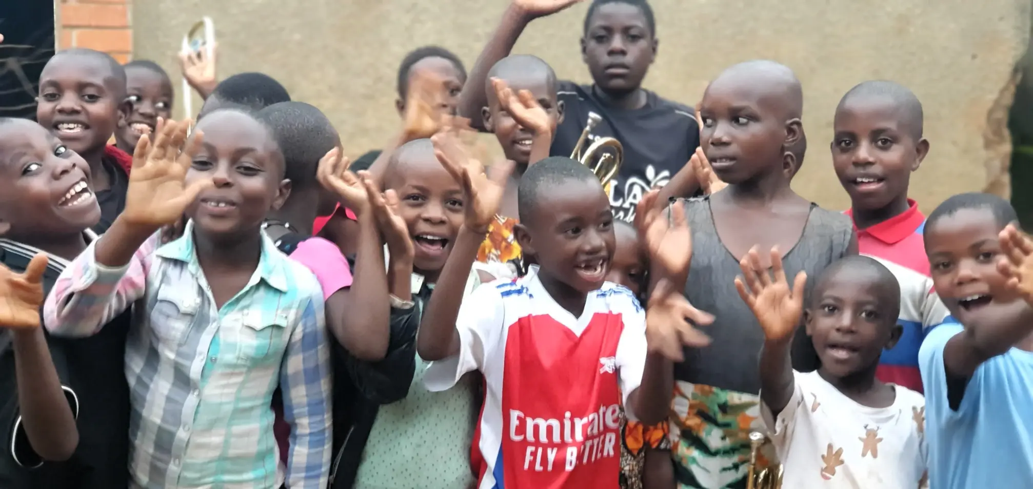 Smiling children at the Educate Brass Foundation in Uganda waving during a community music education session.