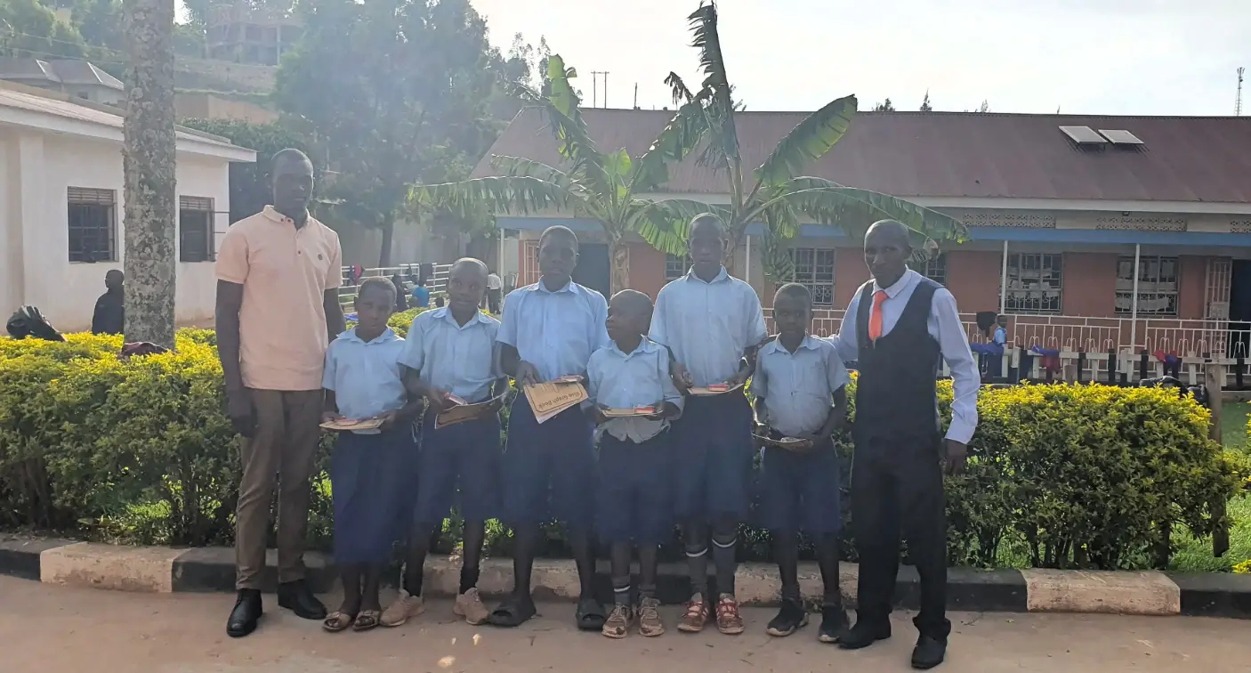 Teachers and students from the Educate Brass Foundation in Uganda standing together outside the school with certificates and notebooks.