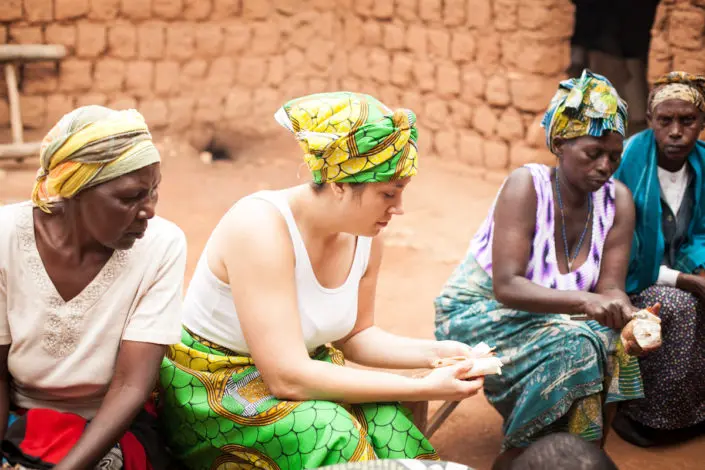 Volunteer cooking with local Ugandan women outside a brick home in Fort Portal during a PLANE Uganda community visit.