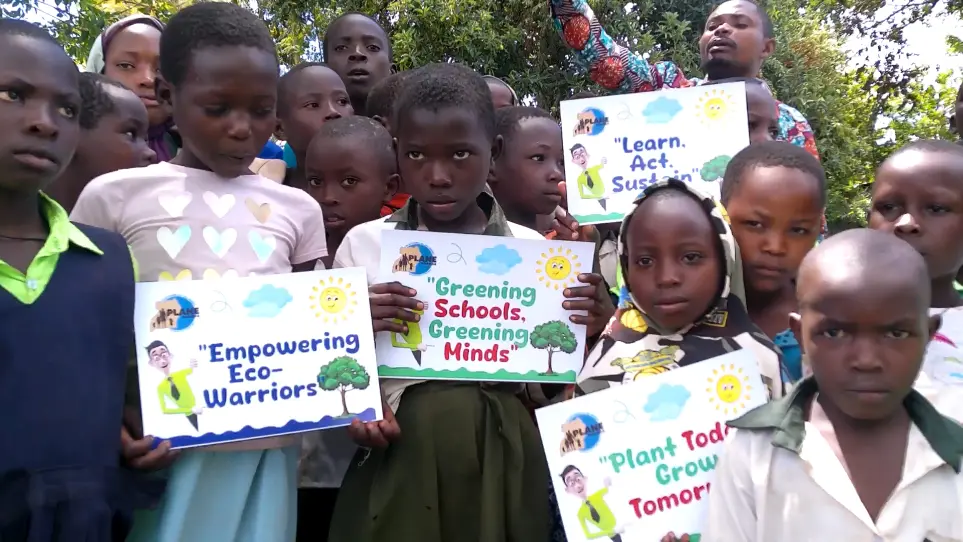 Ugandan pupils hold colorful posters reading “Empowering Eco-Warriors,” “Greening Schools, Greening Minds,” “Learn. Act. Sustain.” and “Plant Today, Grow Tomorrow” during a PLANE Uganda school activity.