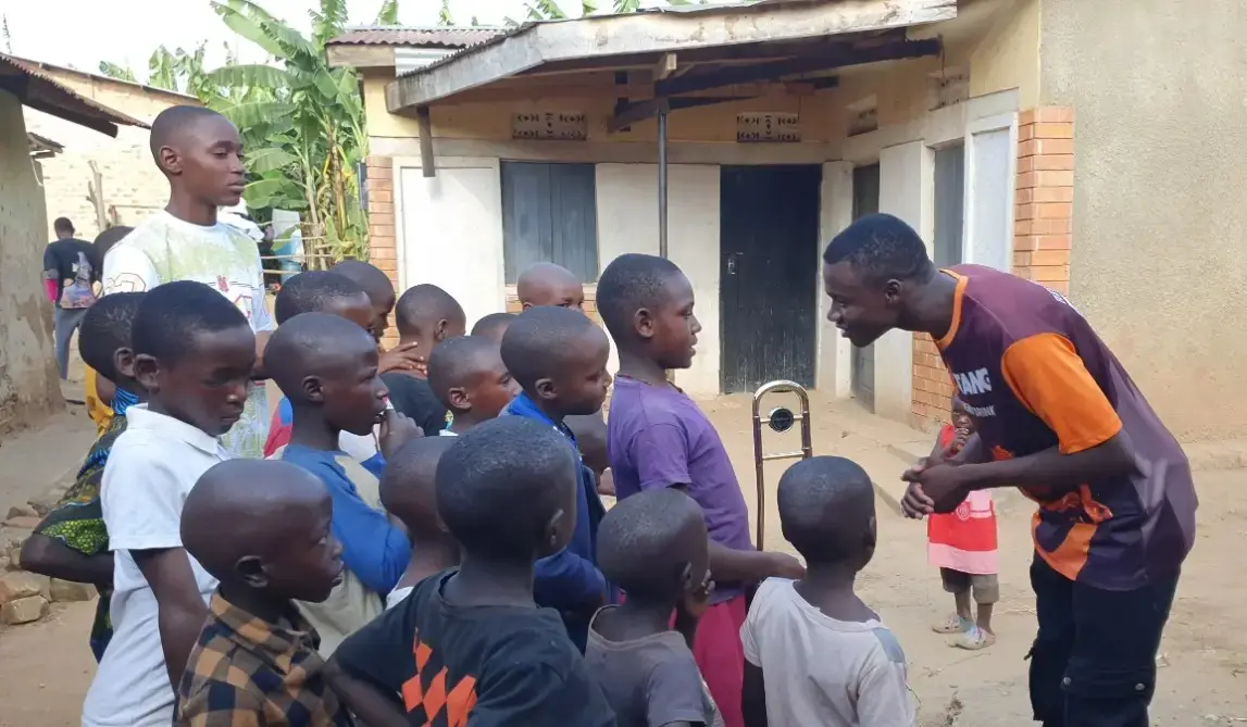 Instructor guiding children during an outdoor trombone lesson at the Educate Brass Foundation in Shuuku Sheema, Uganda.