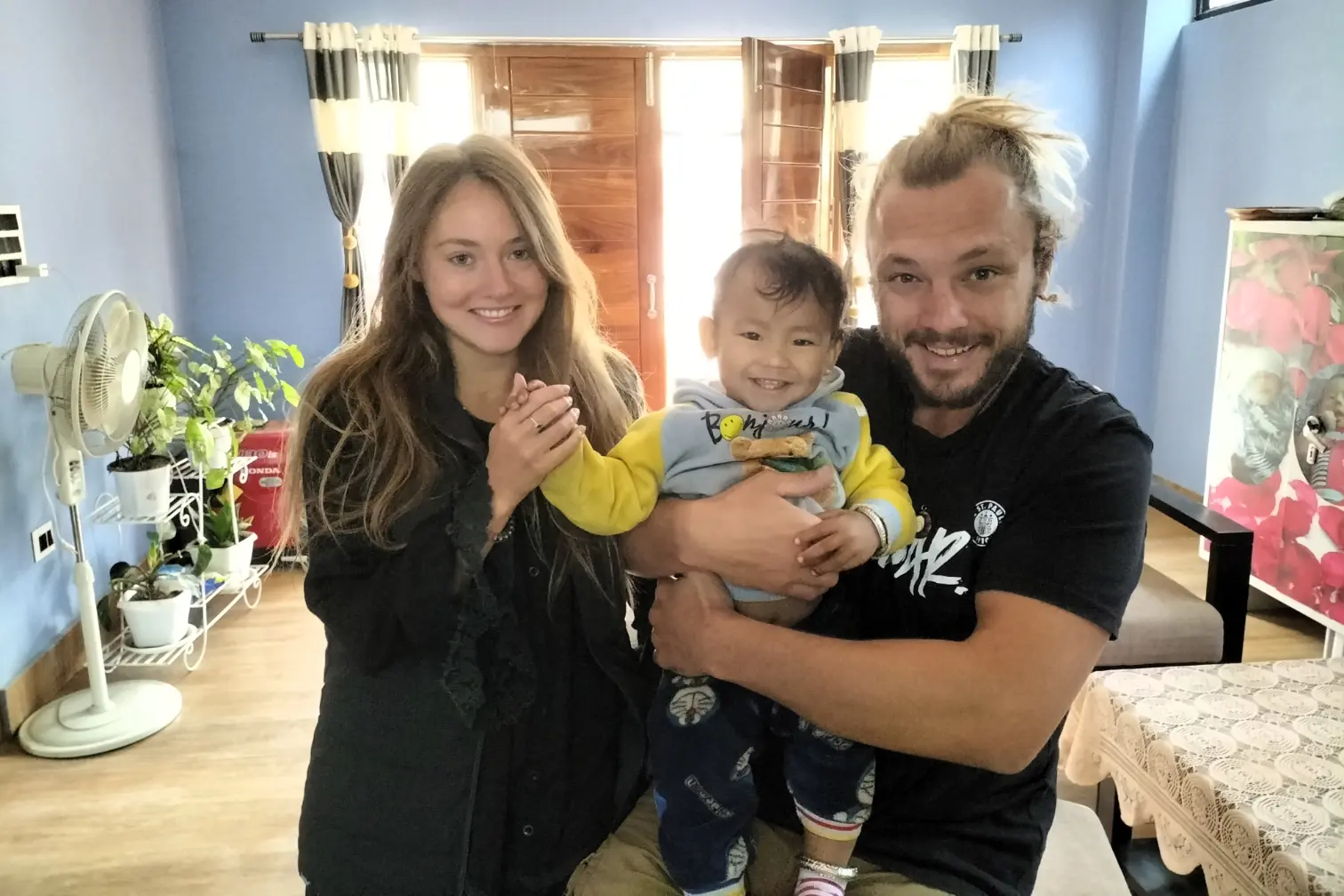 Volunteer in Manipur India at Langon Sanglen: smiling volunteers with a local family and baby inside a welcoming home near Imphal.