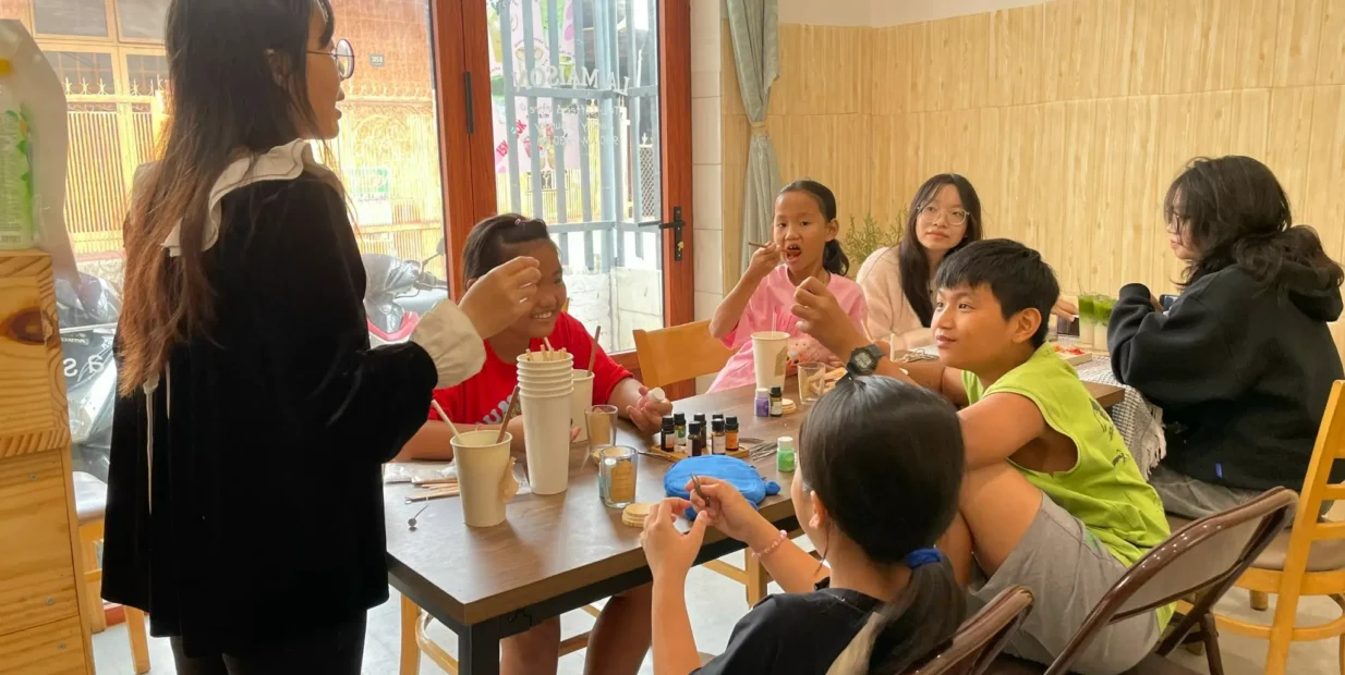 Teacher leading a small English class with Vietnamese children in Dong Nai, Vietnam, showing a friendly homestay volunteer project that offers free meals and accommodation and focuses on cultural exchange.