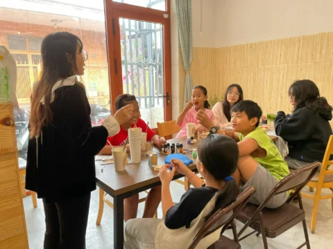 Teacher leading a small English class with Vietnamese children in Dong Nai, Vietnam, showing a friendly homestay volunteer project that offers free meals and accommodation and focuses on cultural exchange.