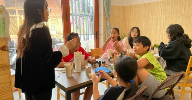 Teacher leading a small English class with Vietnamese children in Dong Nai, Vietnam, showing a friendly homestay volunteer project that offers free meals and accommodation and focuses on cultural exchange.