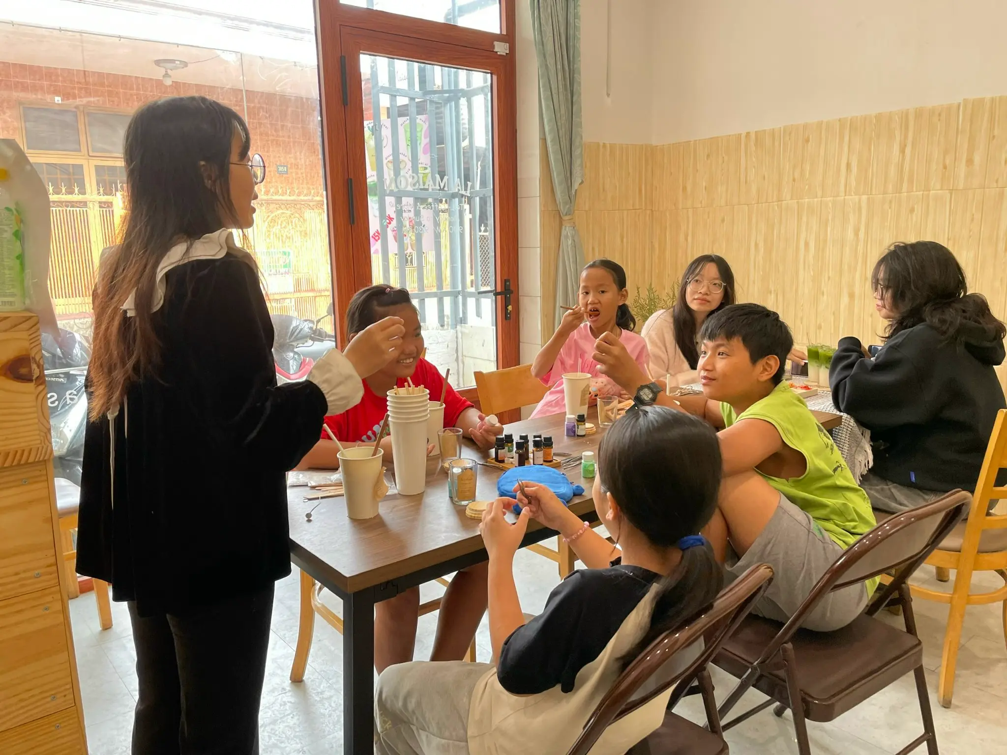 Teacher leading a small English class with Vietnamese children in Dong Nai, Vietnam, showing a friendly homestay volunteer project that offers free meals and accommodation and focuses on cultural exchange.