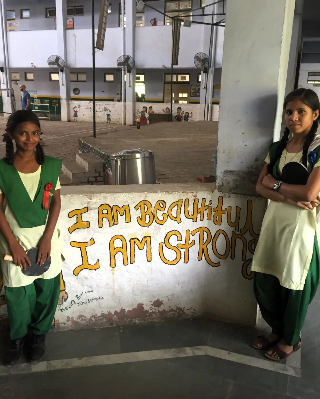 Girls empowerment wall at a school in Anupshahr, Uttar Pradesh, India, with two students in green uniforms and the message “I am beautiful, I am strong” promoting a volunteer project in India