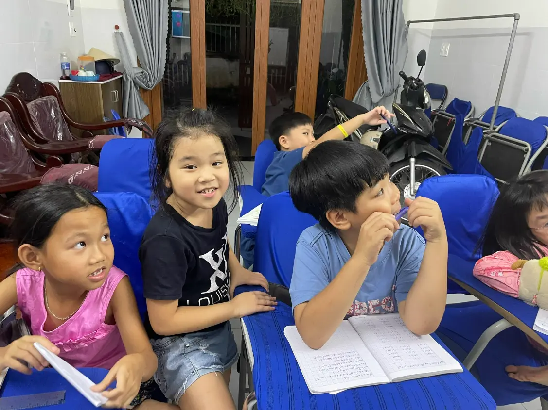 Vietnamese children studying in a small homestay English class in Dong Nai, Vietnam, smiling with notebooks open; image for “Teach English in Dong Nai, Vietnam” volunteer homestay offering free meals and accommodation.