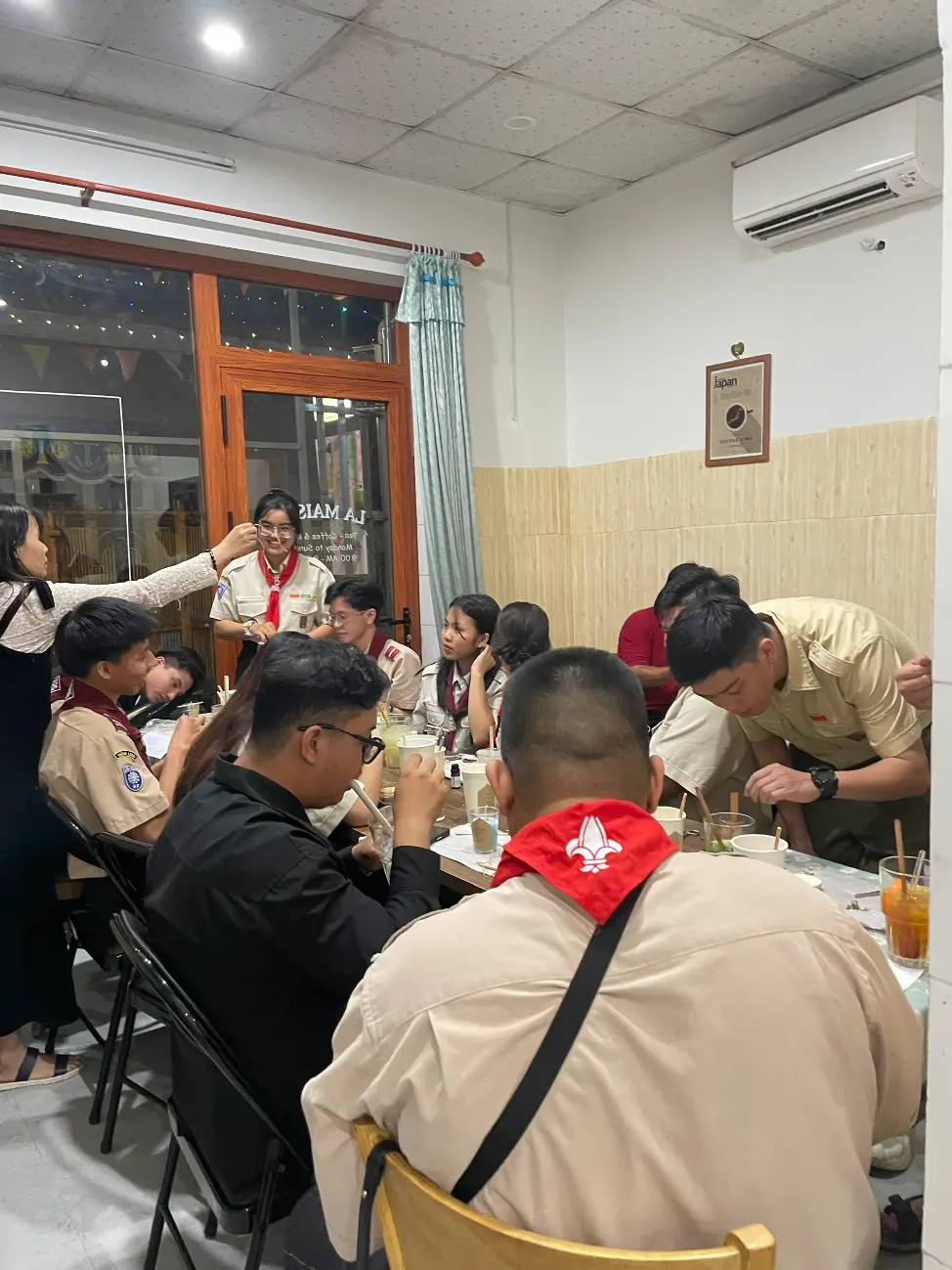 Vietnamese youth group in uniform attending an evening English and culture session in Dong Nai, Vietnam, gathered around tables with drinks and worksheets; image for “Teach English in Dong Nai, Vietnam” volunteer homestay.