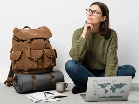 Woman in glasses sits cross-legged with a laptop, backpack and notebook, thinking about accepting paid guest posts.
