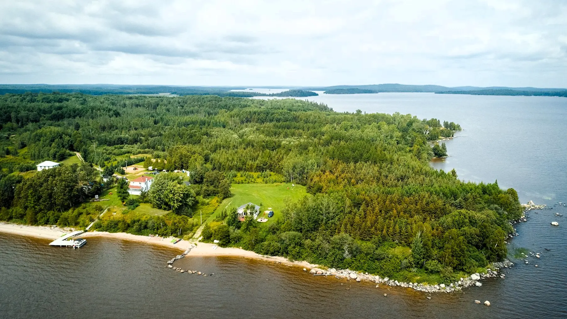 Drone view of a forested lakeside lodge and cabin property in Quebec, Canada, for a hospitality exchange volunteer project