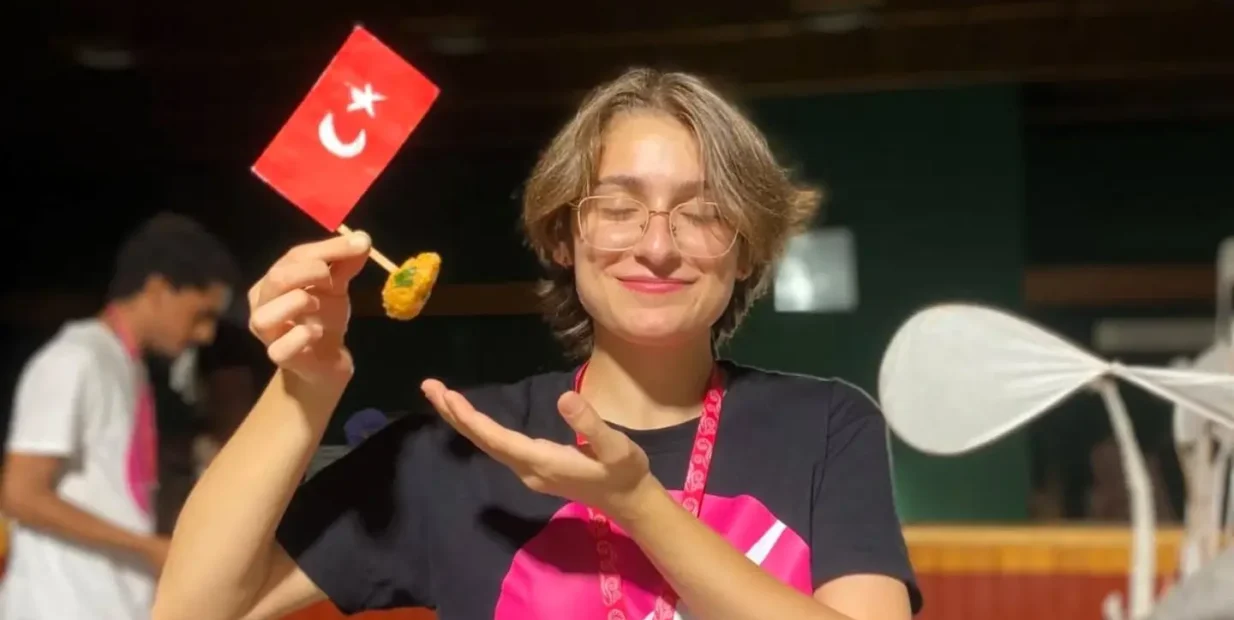 Smiling ESC volunteer holding a small Turkish flag and local food at an English immersion youth camp in Siirt, part of ESC volunteering in Turkey with CEDID Association.