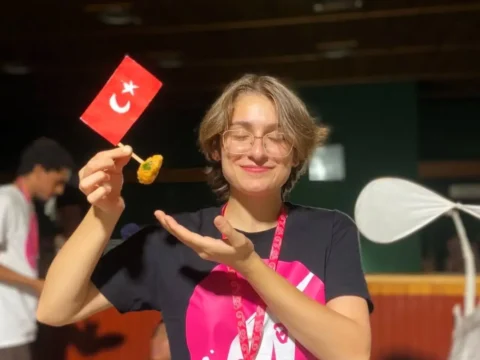 Smiling ESC volunteer holding a small Turkish flag and local food at an English immersion youth camp in Siirt, part of ESC volunteering in Turkey with CEDID Association.