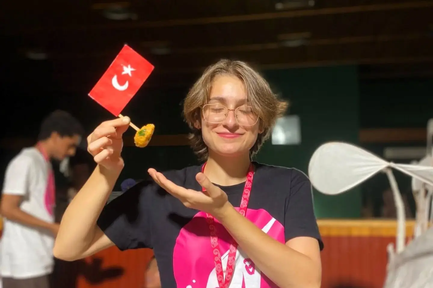Smiling ESC volunteer holding a small Turkish flag and local food at an English immersion youth camp in Siirt, part of ESC volunteering in Turkey with CEDID Association.
