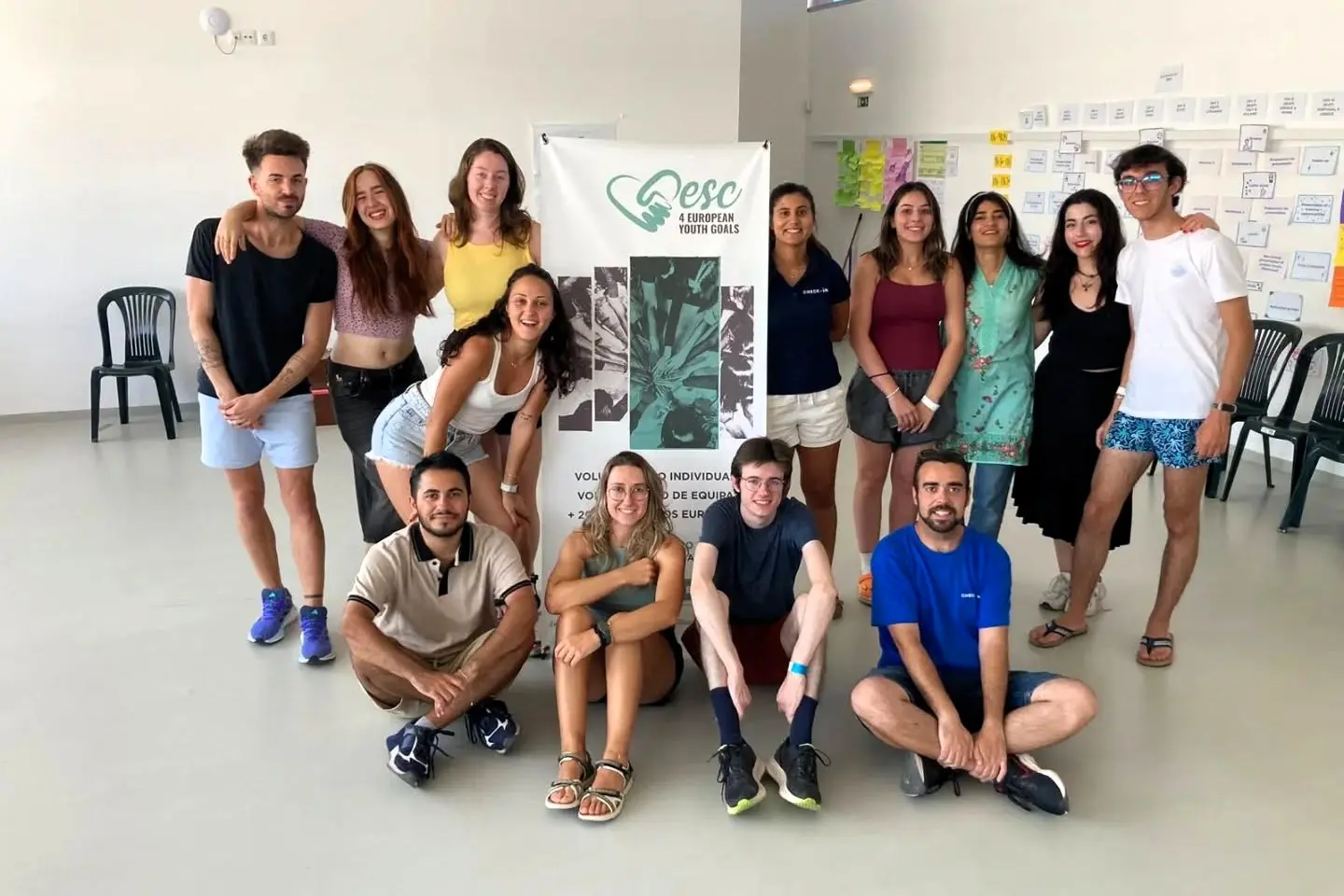 Group of international ESC volunteers posing for a group photo in a workshop room during an ESC project in Turkey, with a banner for European youth goals behind them.