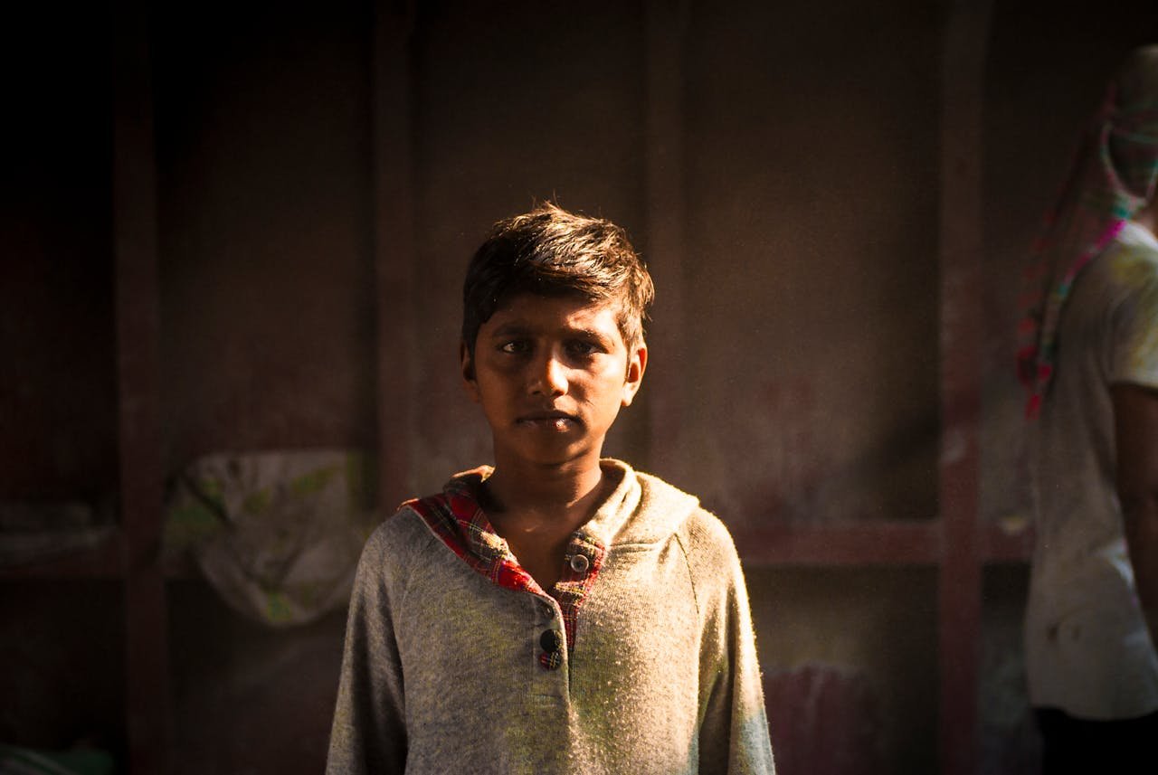 Portrait of a child standing indoors in warm light, used to discuss the orphanage business and orphanage tourism.