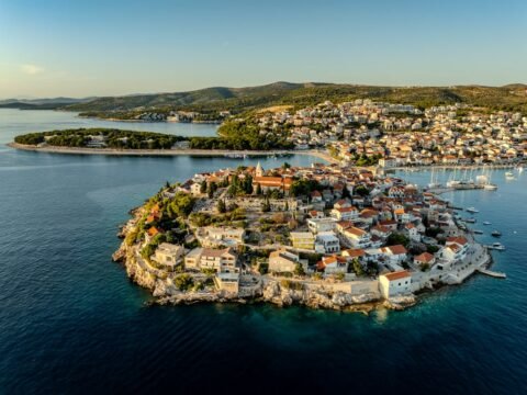 Aerial view of Primošten old town peninsula in Šibenik-Knin County, Croatia, with red-roofed houses, the Church of St. George and the Adriatic Sea.