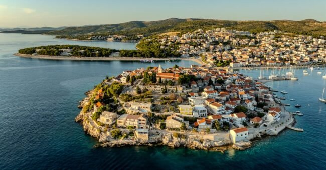 Aerial view of Primošten old town peninsula in Šibenik-Knin County, Croatia, with red-roofed houses, the Church of St. George and the Adriatic Sea.