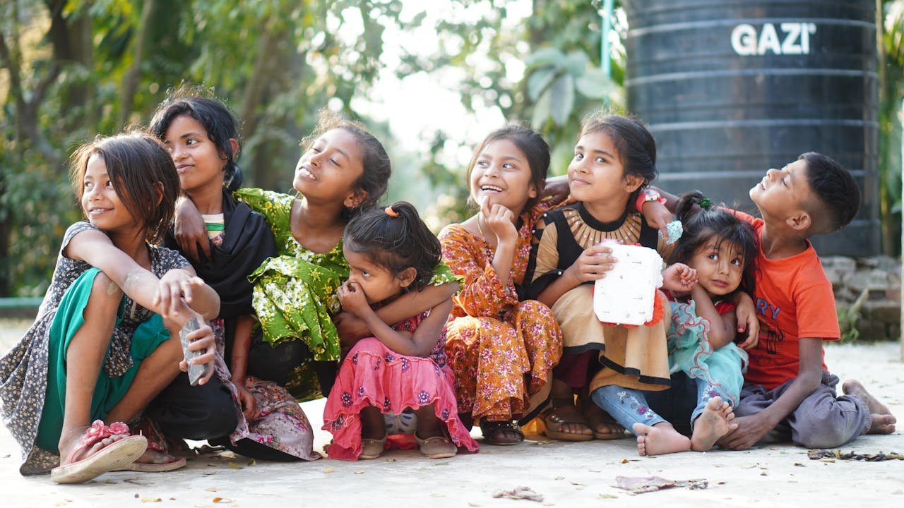 Group of children sitting together outdoors, smiling and looking up, illustrating volunteering with children safer alternatives focused on child safeguarding and community-based support.
