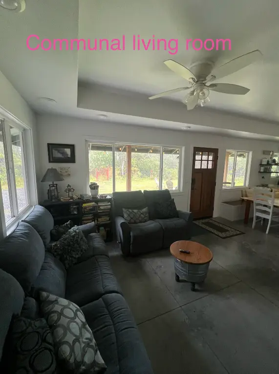 Communal living room at women only work exchange Hawaii in Volcano, featuring sofas, windows overlooking rainforest and shared indoor space.