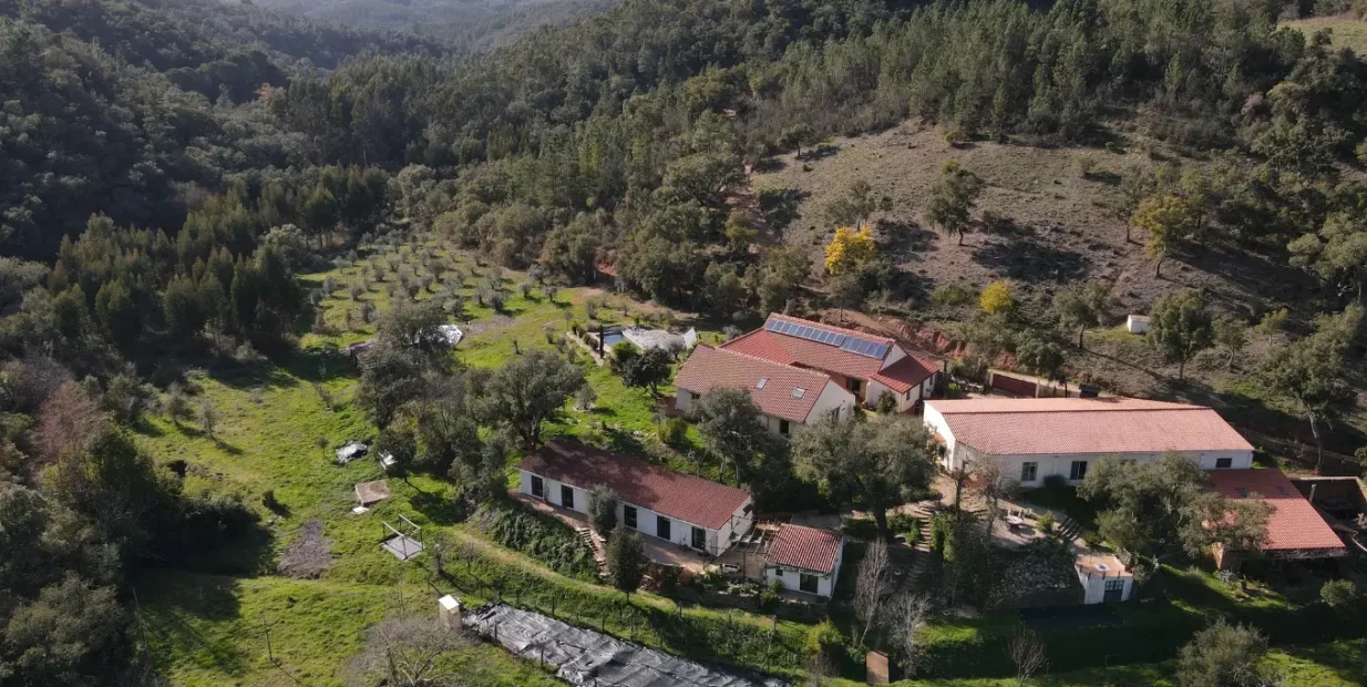 Aerial view of Satvana rural retreat buildings in a green valley near Amoreiras, southern Portugal.