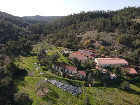 Aerial view of Satvana rural retreat buildings in a green valley near Amoreiras, southern Portugal.