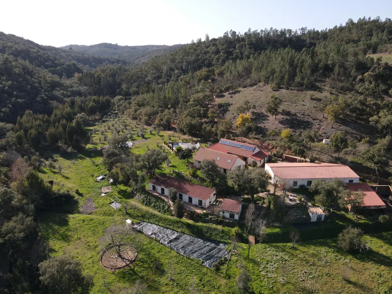 Aerial view of Satvana rural retreat buildings in a green valley near Amoreiras, southern Portugal.