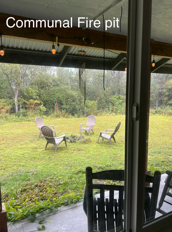 Communal outdoor fire pit area at Volcano Hawaii women work trade, showing chairs on grassy backyard in quiet rainforest setting.