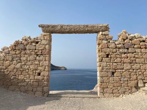 Stone doorway in a rugged old wall framing a view of the blue sea and cliffs on Milos island, Cyclades, Greece.