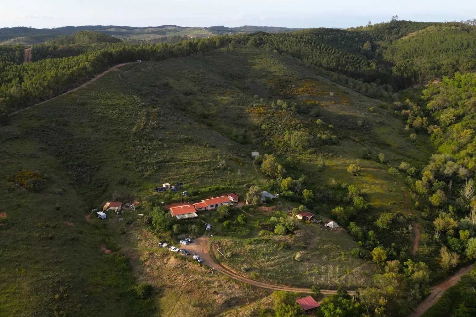Aerial view of Luna Solua off grid family farm in Alentejo, Portugal, surrounded by forested hills, rural tracks, gardens and open land where volunteers help with natural building, gardening and rural life projects.