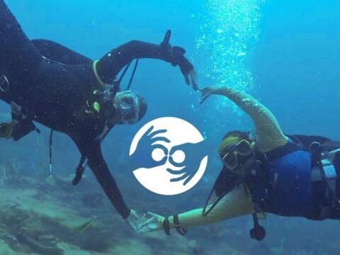Two volunteer scuba divers underwater in the Philippines forming a heart shape around the Marine Conservation Philippines logo