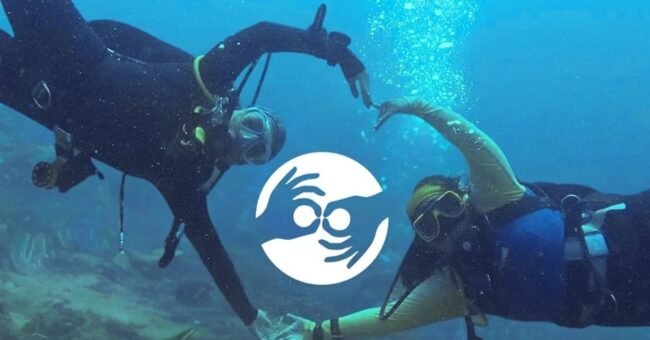 Two volunteer scuba divers underwater in the Philippines forming a heart shape around the Marine Conservation Philippines logo