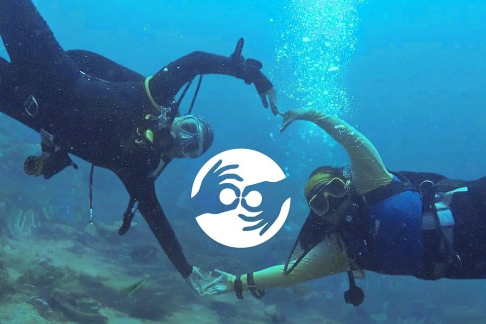 Two volunteer scuba divers underwater in the Philippines forming a heart shape around the Marine Conservation Philippines logo