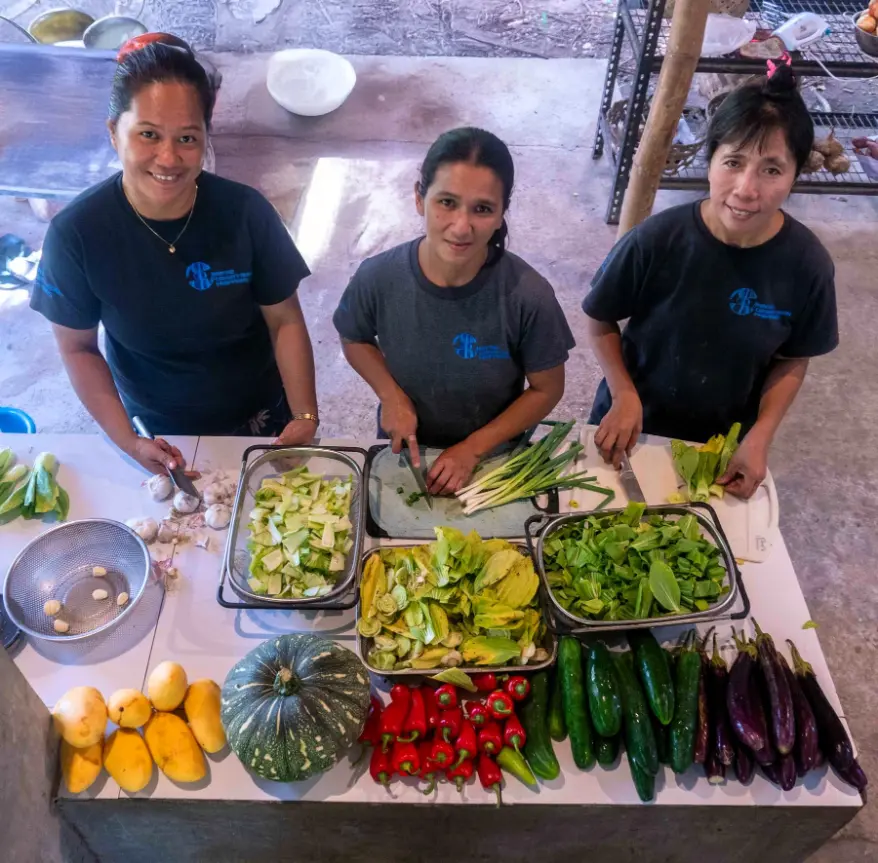 Three Marine Conservation Philippines staff members preparing fresh vegetables and fruit for shared meals at the project site