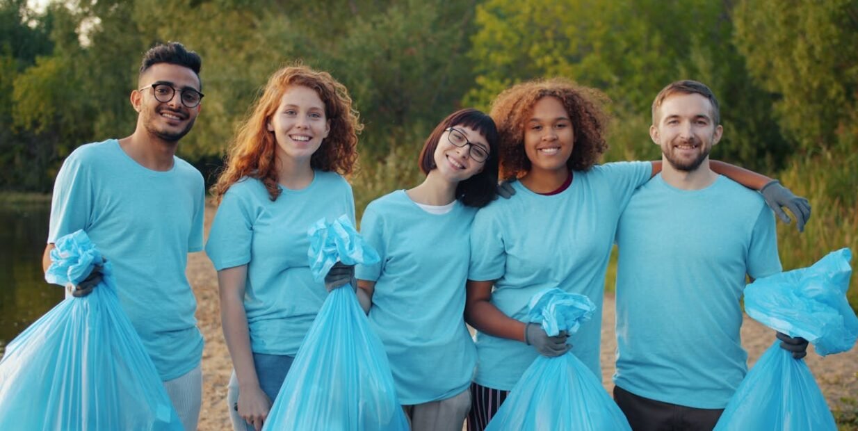 Group of young volunteers holding trash bags during an outdoor community clean-up in a natural park setting
