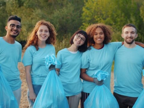 Group of young volunteers holding trash bags during an outdoor community clean-up in a natural park setting