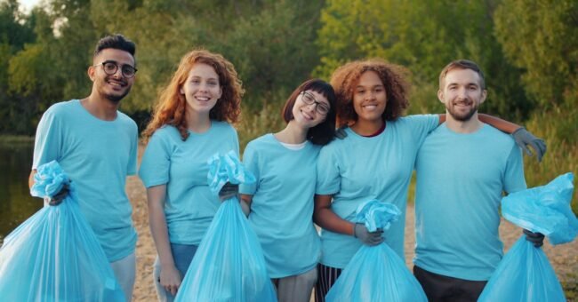 Group of young volunteers holding trash bags during an outdoor community clean-up in a natural park setting