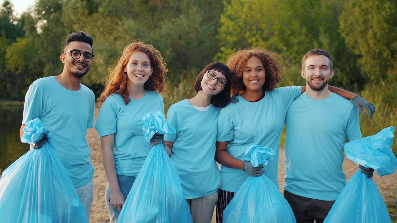 Group of young volunteers holding trash bags during an outdoor community clean-up in a natural park setting