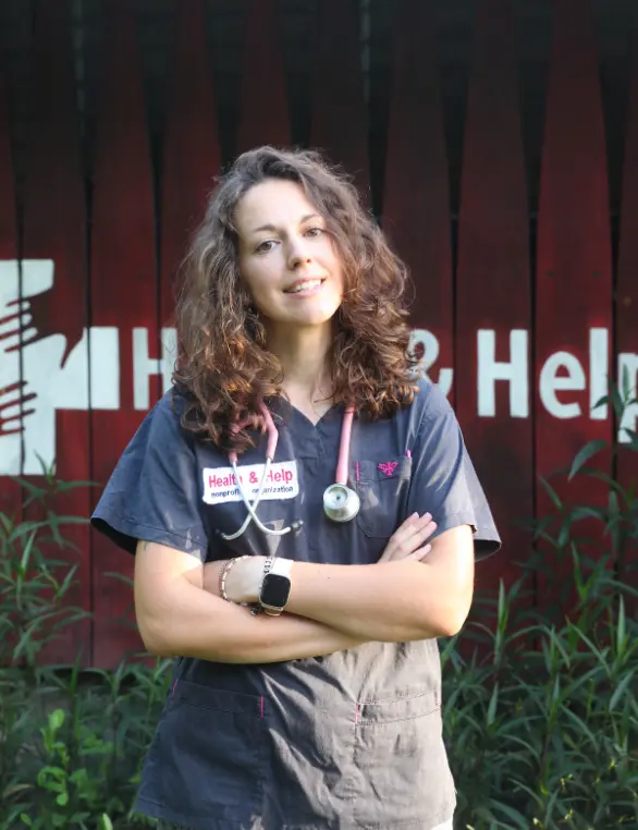 Health & Help medical volunteer in scrubs with a stethoscope outside a rural healthcare clinic in Guatemala, supporting community health services in Totonicapán.