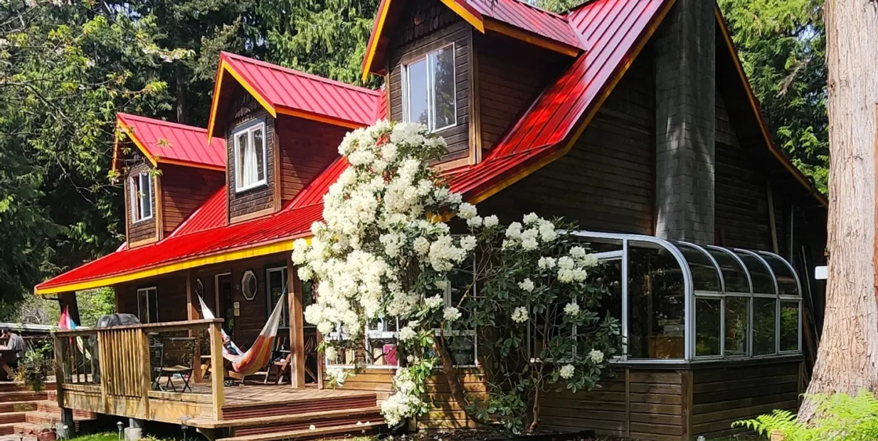 ooden hostel-style lodge with a red roof, forest surroundings and flowering shrubs in Roberts Creek, British Columbia, for a volunteer exchange on Canada’s Sunshine Coast.