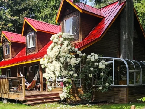 ooden hostel-style lodge with a red roof, forest surroundings and flowering shrubs in Roberts Creek, British Columbia, for a volunteer exchange on Canada’s Sunshine Coast.