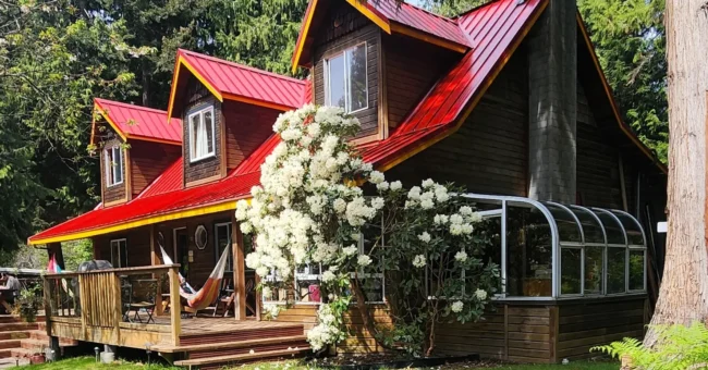 ooden hostel-style lodge with a red roof, forest surroundings and flowering shrubs in Roberts Creek, British Columbia, for a volunteer exchange on Canada’s Sunshine Coast.
