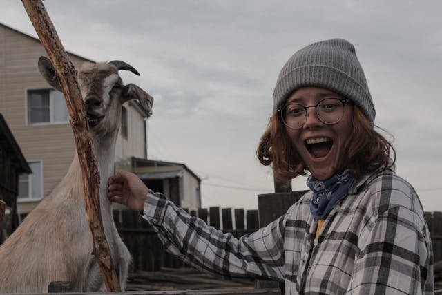 Young volunteer petting a goat at a farm, illustrating the need for safety rules and awareness of animal behaviour during volunteer work.