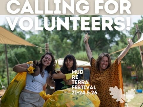 Three smiling volunteers at Spirala EcoVillage in Idanha-a-Nova, Portugal, with bags and a wheelbarrow during the volunteer call for Mud Re Terra Festival 2026.