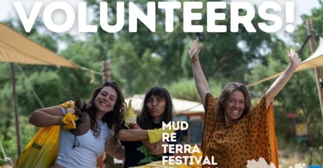 Three smiling volunteers at Spirala EcoVillage in Idanha-a-Nova, Portugal, with bags and a wheelbarrow during the volunteer call for Mud Re Terra Festival 2026.