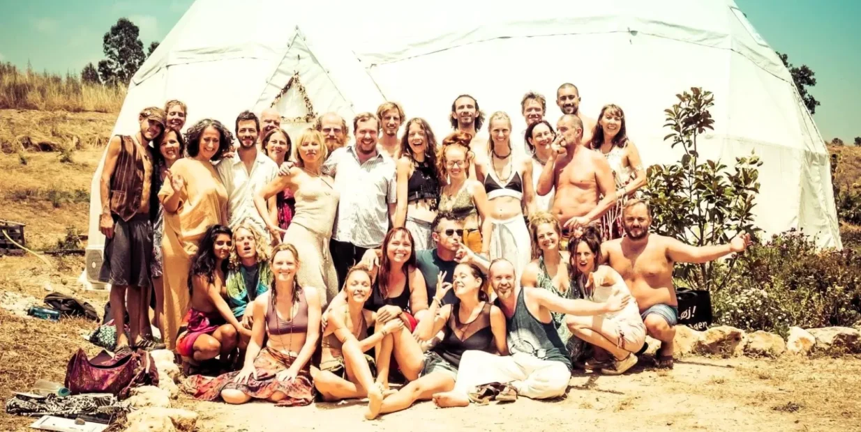 Group of volunteers smiling in front of a white retreat dome at a reforestation and land rehabilitation project in the Algarve, Portugal.