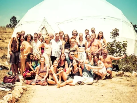 Group of volunteers smiling in front of a white retreat dome at a reforestation and land rehabilitation project in the Algarve, Portugal.
