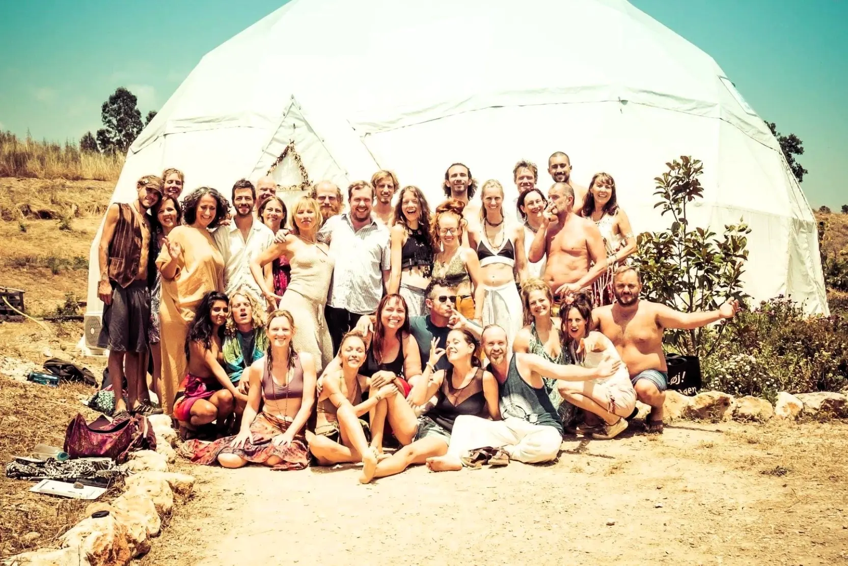 Group of volunteers smiling in front of a white retreat dome at a reforestation and land rehabilitation project in the Algarve, Portugal.