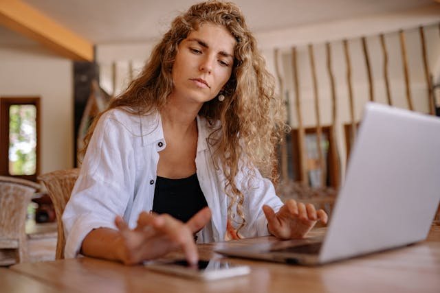 Young woman using a laptop and phone to share her volunteer travel plans and location with someone she trusts before a volunteer exchange.