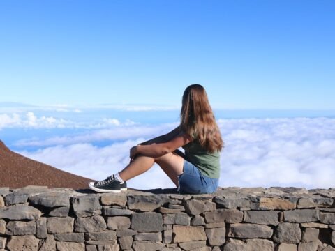 Young traveler sitting above the clouds, representing independent travel websites, slow travel and thoughtful travel planning.